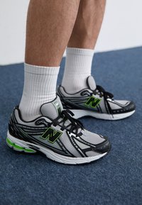 Baskets de sport noires et grises avec tige en maille, accents verts et semelle en caoutchouc. Inclut des lacets noirs et des chaussettes blanches mi-mollet.