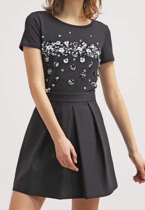 Schwarzes Kleid mit kurzen Ärmeln, verzierten Oberteil mit weißen und silbernen Blumen-Pailletten, tailliert und mit ausgestelltem, plissiertem Rock.
