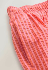 Pantalones cortos color coral con rayas verticales en un tono más claro. Presentan una cintura elástica y detalles de tejido texturizado.