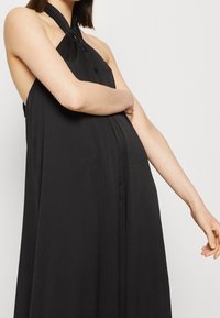 Abito nero senza maniche realizzato in tessuto leggero, con scollatura annodata, silhouette fluida e una leggera texture.