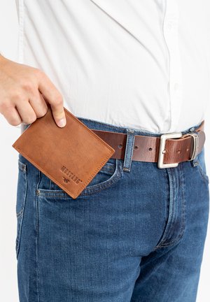 Brown leather wallet with a pebbled texture, partially inserted into blue denim jeans. Silver belt buckle visible. Simple, rectangular design.
