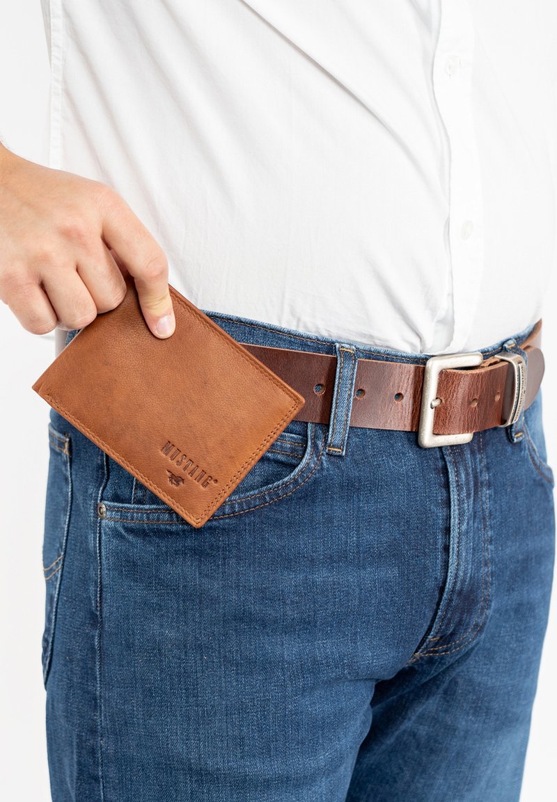 Brown leather wallet with a pebbled texture, partially inserted into blue denim jeans. Silver belt buckle visible. Simple, rectangular design.