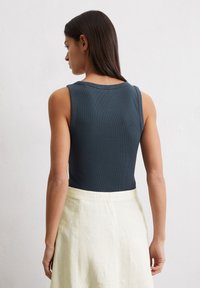 Débardeur côtelé bleu foncé à col rond, associé à une jupe en lin de couleur claire, affichant une coupe décontractée et un design épuré.