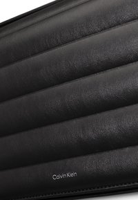 Borsa a mano in pelle nera con un design trapuntato, con cuciture diagonali e un logo stampato sul davanti. La superficie testurizzata aggiunge profondità.