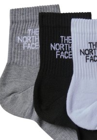 Kolme paria polvenkorkuisia sukkia harmaana, mustana ja valkoisena, joissa on raidoitettu pinta ja "THE NORTH FACE" -logo erottuvalla valkoisella kirjoituksella.
