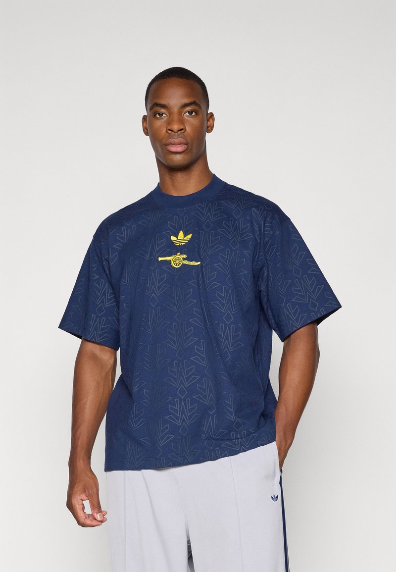 Camiseta de manga corta azul marino con una textura sutil y un logo amarillo de Adidas con un diseño gráfico en el pecho.