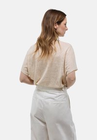 Haut beige à manches courtes en tissu léger et texturé, associé à un pantalon taille haute de couleur crème avec poches latérales.