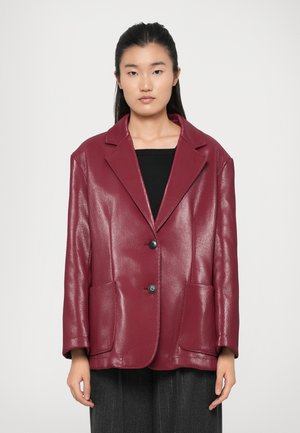 Blazer in eco-pelle bordeaux con collo strutturato, due tasche frontali e due bottoni. Finitura liscia e lavorata. Maniche ampie.