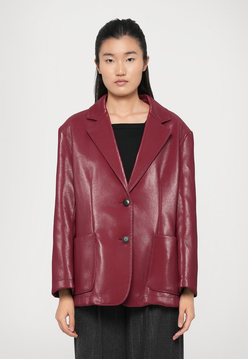 Blazer in eco-pelle bordeaux con collo strutturato, due tasche frontali e due bottoni. Finitura liscia e lavorata. Maniche ampie.