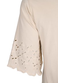 Blusa di cotone beige con motivi a foglia ricamati e dettagli a taglio sulle maniche svasate. Tessuto morbido e orlo a scallop.