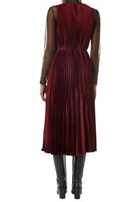 Burgunderfarbenes, gefaltetes Kleid mit einer strukturierten Überlagerung, das über einen Taillengürtel und einen Schlüsselrücken verfügt. Kombiniert mit kniehohen schwarzen Stiefeln.