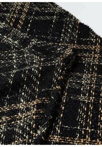 Tissu noir texturé avec un motif tissé de fils beiges et blanc cassé formant un motif en grille.