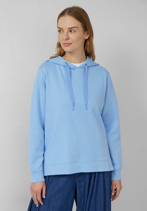 Haut à capuche bleu clair avec un cordon de serrage, manches longues et poignets côtelés. Tissu doux avec une coupe décontractée, associé à un pantalon en denim foncé.