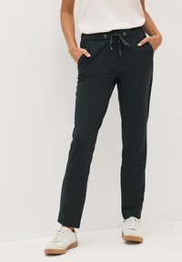 Pantalons de jogging légers de couleur vert foncé avec une taille élastique à cordon, poches latérales, jambes fuselées et texture douce, associés à des baskets blanches.