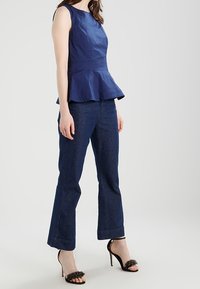 Marinblå peplumtop med en strukturerad bodice, tillsammans med mörkblå utsvängda jeans. Svarta klacksandaler med pärlliknande dekorationer.