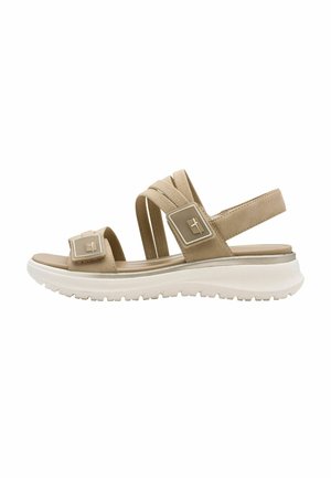 Beige sandal with wide elastic straps, adjustable hardware accents, and a textured white sole for grip. Casual, lightweight design.
