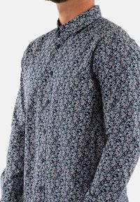 Bloemenpatroon overhemd met knopen in marineblauw, met kleine witte en rode bloemen, duurzame stof, getailleerde kraag en knopen aan de voorkant.