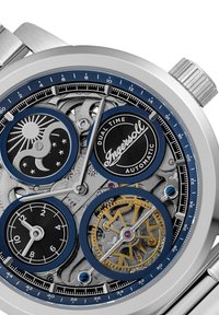 Roestvrijstalen horloge met blauwe accenten, met een skeleton wijzerplaat en indicatoren voor dubbele tijdzones. Beschikt over ingewikkelde tandwielen en details.