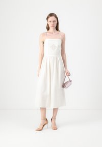 Vestido blanco sin mangas con escote cuadrado y detalle de diamantes bordados. Diseño fluido, cintura ceñida, combinado con un bolso lavanda y tacones nude.