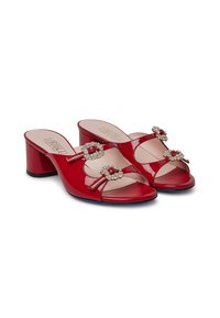 Mule con tacchi in vernice rossa con punta aperta. Ogni scarpa presenta due gioielli decorativi sulle cinghie, con un tacco a blocco basso.
