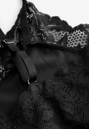 Zwarte kanten bralette met bloemmotieven, een gladde stofbasis, verstelbare bandjes en een gedetailleerde kantafwerking langs de halslijn.