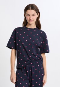 Námořnické bavlněné tričko s krátkým rukávem, zdobené vzorem malých růžových srdcí. Uvolněný střih a měkká textilie, ideální pro každodenní nošení.