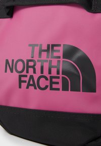 Rózsaszín nylon táska fekete logóval, amelyen egy negyedkör és a "THE NORTH FACE" felirat található; fekete alappal és strapabíró pántokkal rendelkezik.