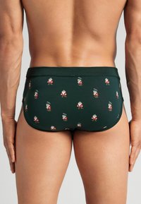 Gröna simbriefar med ett upprepande mönster av tecknade karaktärer i röd och vit; tillverkade av stretchigt tyg med en slät textur.