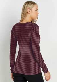 Pitkähihaisen paidan maroon-värinen pohja, jossa on ohuita pystysuoria uria. Pehmeä kangas, pukeutuva muotoilu, pyöreä pääntie ja sileä pinta.