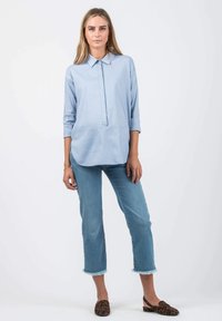 Himmelblaues, knöpfbares Hemd mit Kragen und Dreiviertelärmeln. Kombiniert mit verkürzten Jeans mit fransigem Saum und braunen, leopardenmusterierten Ballerinas.