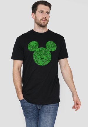 Schwarzes Baumwoll-T-Shirt mit grünem floralen Mickey-Maus-Design. Kurze Ärmel und runder Halsausschnitt. Das Model trägt eng anliegende Jeans.