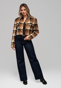 Cropped jakke i slangemønster med nuancer af brun og sort, med to brystlommer og gyldne knapper. Parret med mørkeblå vide bukser.