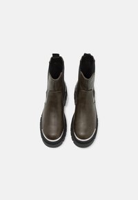 Paire de bottines Chelsea en cuir marron foncé avec semelles noires épaisses et languettes de tirage, vues de dessus sur fond blanc.