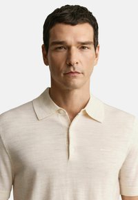 Beige polo shirt met korte mouwen en een kraag, gemaakt van lichte stof. Heeft een knoopsluiting en een subtiele logodetail op de borst.