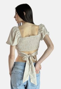 Top corto in gingham crema con maniche a sbuffo, tessuto smock, schiena larga a quadrato e dettaglio a fiocco in vita, abbinato a jeans a vita alta.