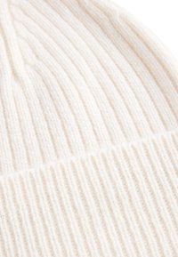 Beanie in morbido cotone crema. Presenta un motivo a coste verticali e una texture liscia e spessa. Design senza cuciture senza hardware visibile.