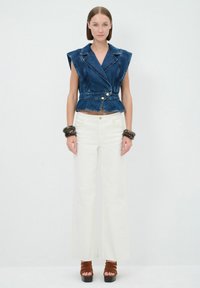 Top in denim con un design sartorial, scollo ampio e vita a peplum; abbinato a pantaloni bianchi a gamba larga e tacchi marroni.