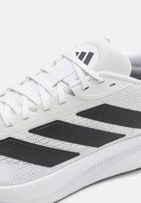 White athletic shoe featuring a mesh upper with black three-stripe logo accents and a textured sole. Designed with a lightweight construction.