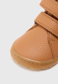 Smeđa kožna cipela s teksturiranim završetkom, s dvije trake na čičak i zaobljenim vrhom. Potplat je gumeni s laganim profilom.