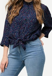 Navy blouse with a tie-front, featuring a small red and beige floral pattern, button-down design, and three-quarter sleeves, paired with light blue jeans.