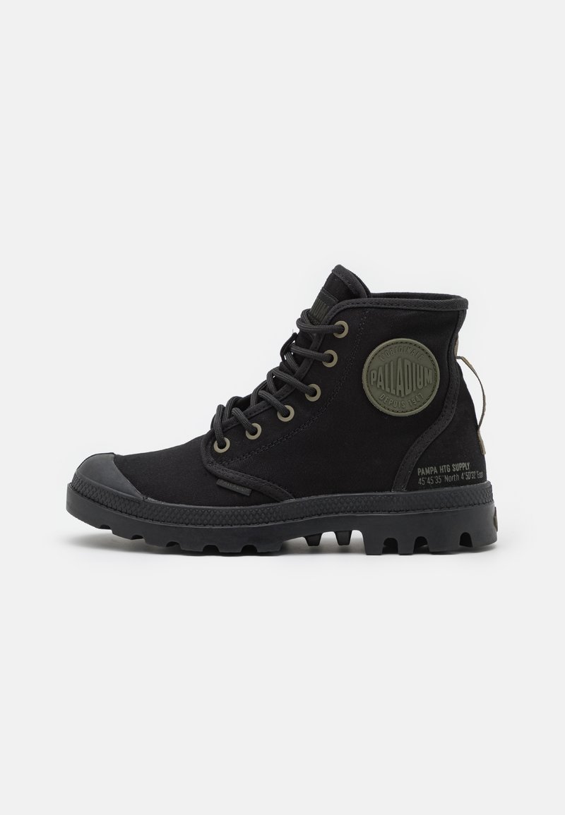 Botas de tobillo de lona negra con puntera de goma, cordones redondos y parche circular con logo en el lateral; suela resistente con tacos de tracción.