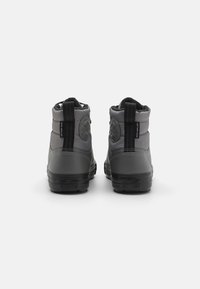 Grå hög sneakers med en slät syntetisk ovandel, svart gummisula, kontrasterande hälflik och cirkulär logotyp på baksidan.