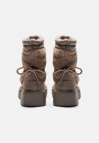 Bottes en fourrure marron avec un haut froncé, bout arrondi et semelle plate à nervures. Présente des accentuations en lacet à l'arrière.