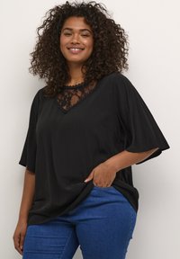 Haut noir avec un col en V et des détails en dentelle au niveau du col ; manches courtes ; tissu léger ; associé à un jean en denim bleu.
