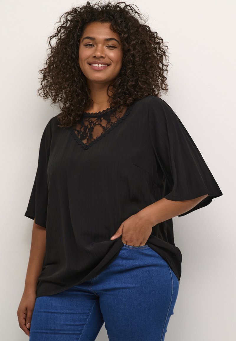 Haut noir avec un col en V et des détails en dentelle au niveau du col ; manches courtes ; tissu léger ; associé à un jean en denim bleu.