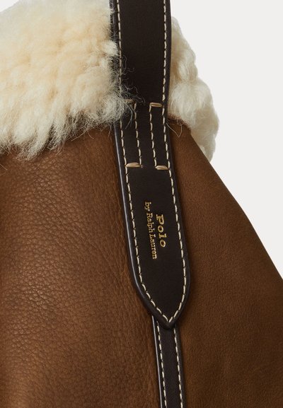 Brun läderhandväska med en fluffig, krämfärgad pälsdetalj, med en mörk läderrem och kontrasterande sömmar. Guldlogotypdetalj finns.