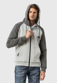 Kapuzensweatshirt in Grau und Hellgrau, mit Reißverschluss, Kängurutaschen und elastischen Bündchen. Weicher, strukturierter Stoff.
