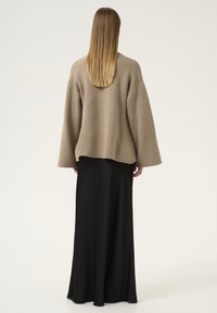 Maglione oversize beige lavorato a maglia con maniche larghe, abbinato a una lunga gonna nera, caratterizzato da una texture liscia e una silhouette fluida.