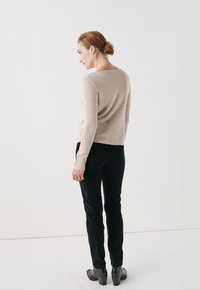 Maglione beige morbido a maniche lunghe, abbinato a pantaloni neri a vestibilità slim e stivali neri con tacco, visto da dietro.