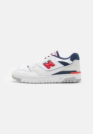 Hvid New Balance 550 sneaker med rød "N"-logo, marineblå accenter, grå sål og hvide snørebånd vist på en ensfarvet baggrund.